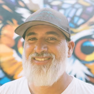 Wes Abarca smiling in front of his stained-glass-style owl mural